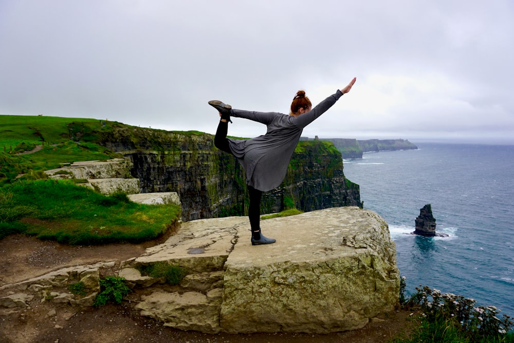 a woman doing a yoga pose on a cliff overlooking the ocean