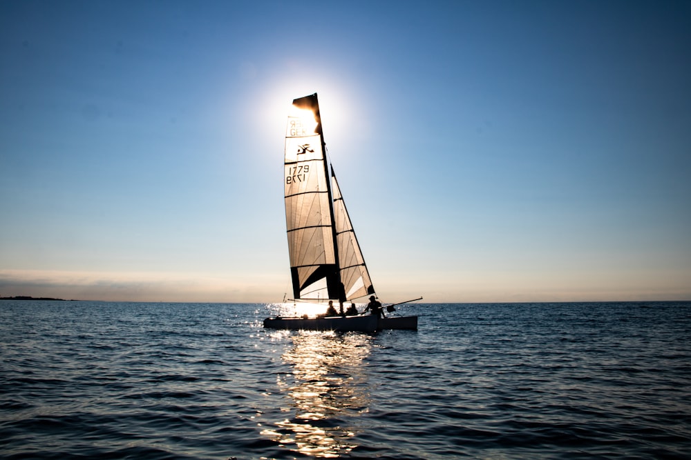 a sailboat sailing on the water with the sun in the background