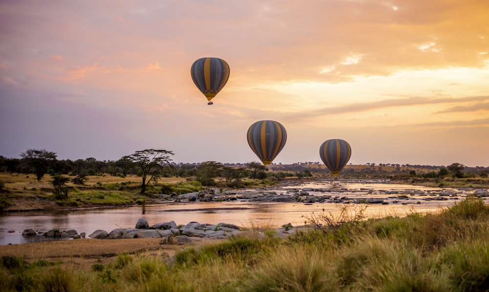 three hot air balloons flying over a river