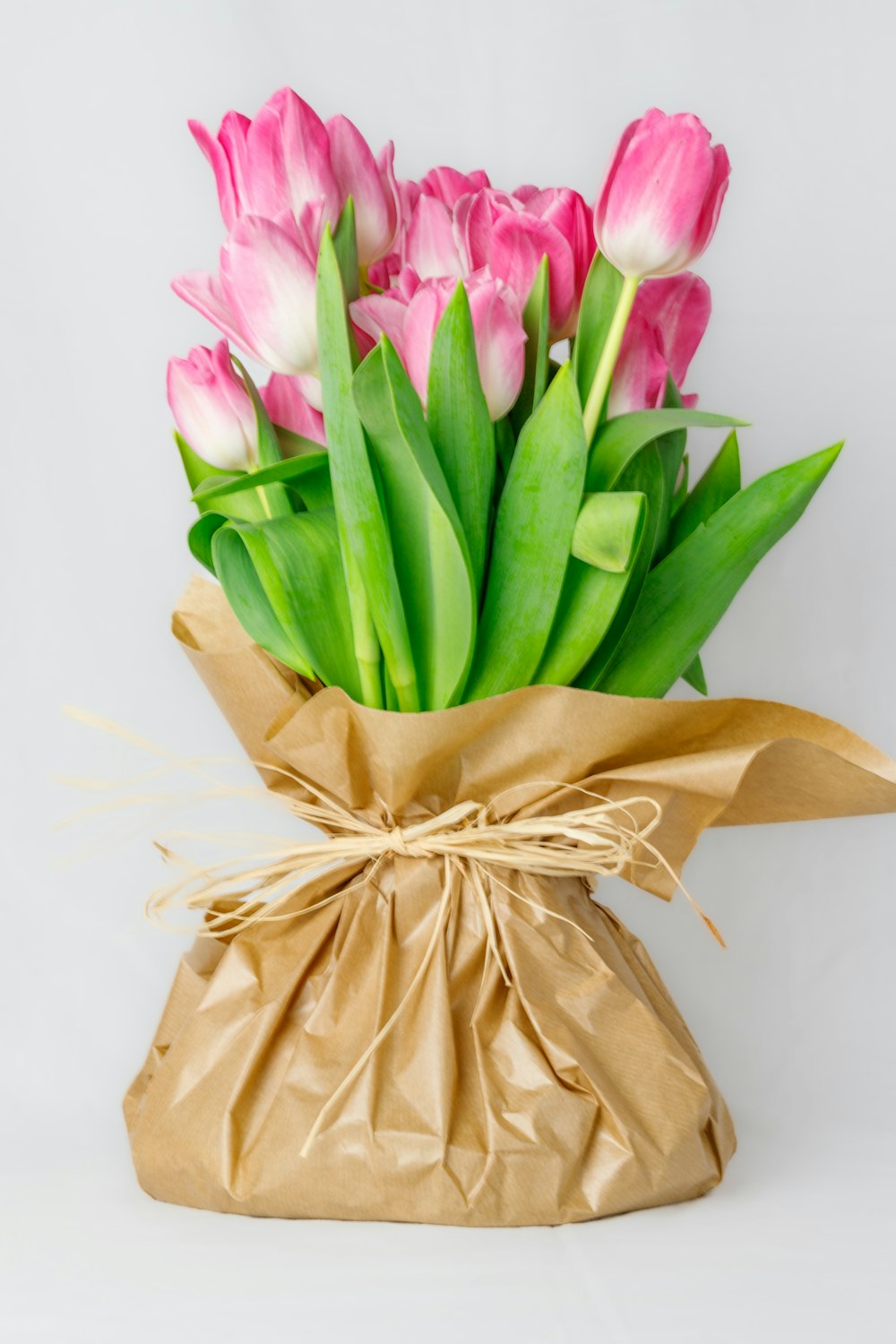 a bouquet of pink and white tulips in a brown paper bag