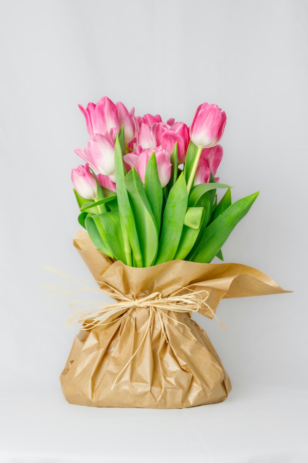 a bouquet of pink and white tulips wrapped in brown paper