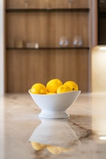 a white bowl filled with lemons on top of a counter