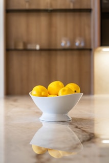 a white bowl filled with lemons on top of a counter