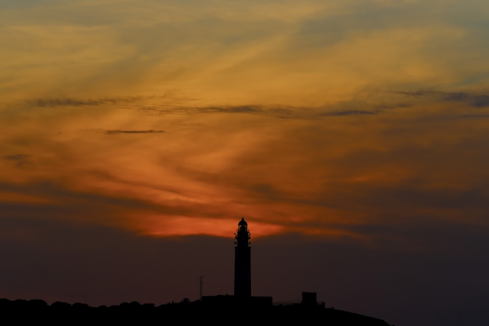 the sun is setting behind a tower with a clock on it