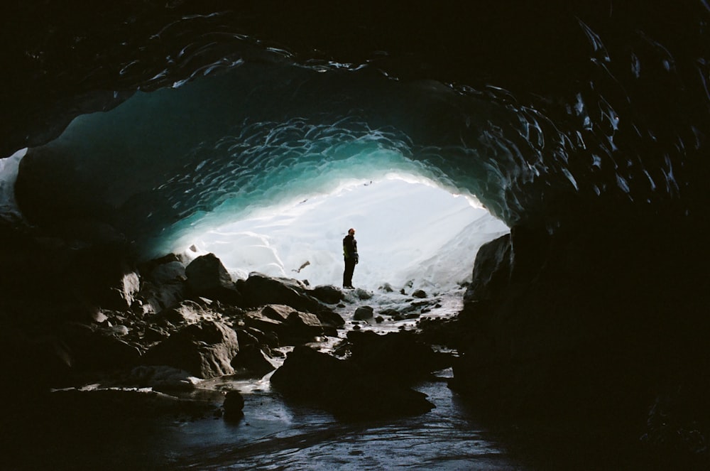 a man standing inside of a cave next to a body of water