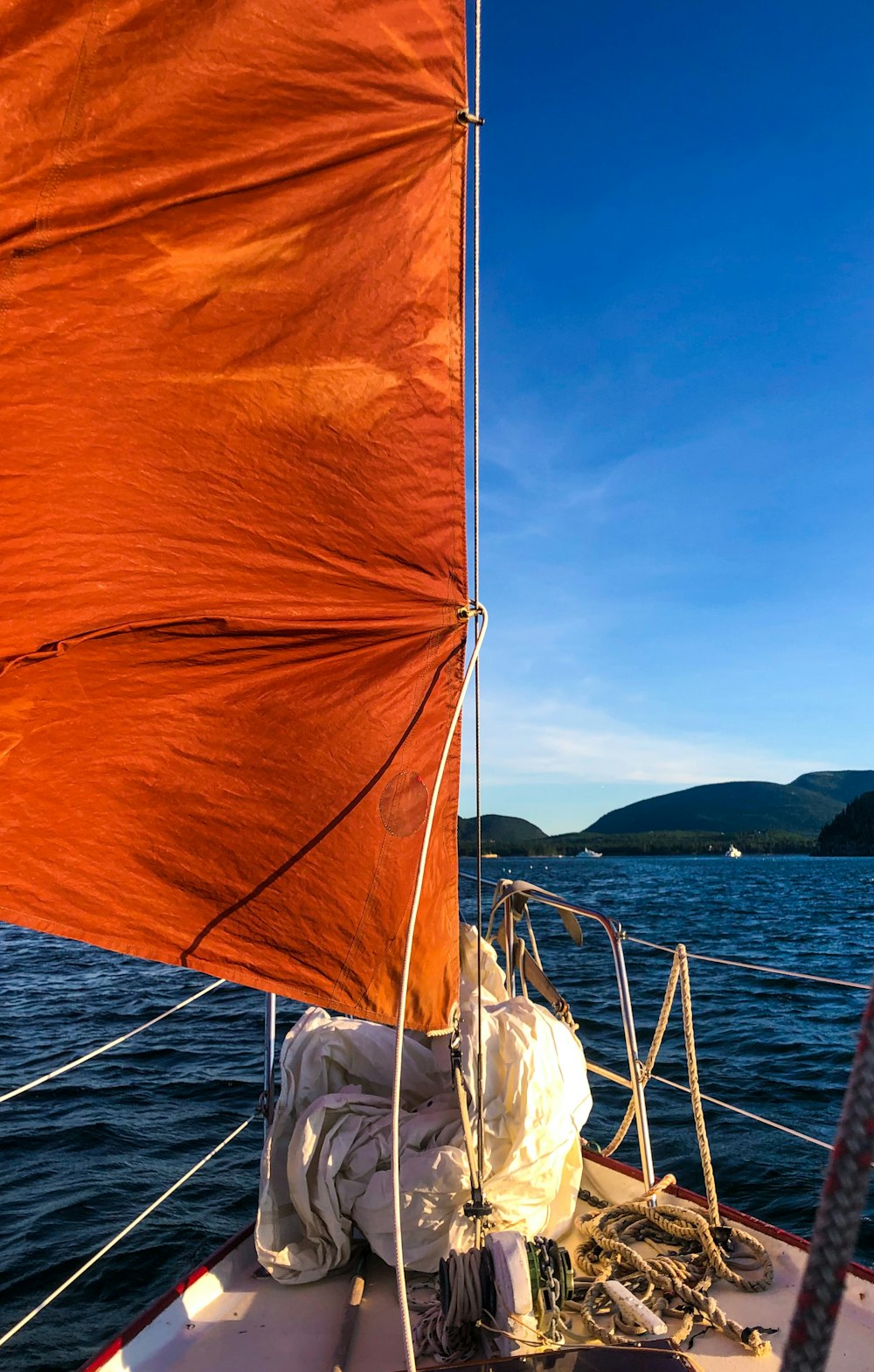 a sailboat with an orange sail on a body of water