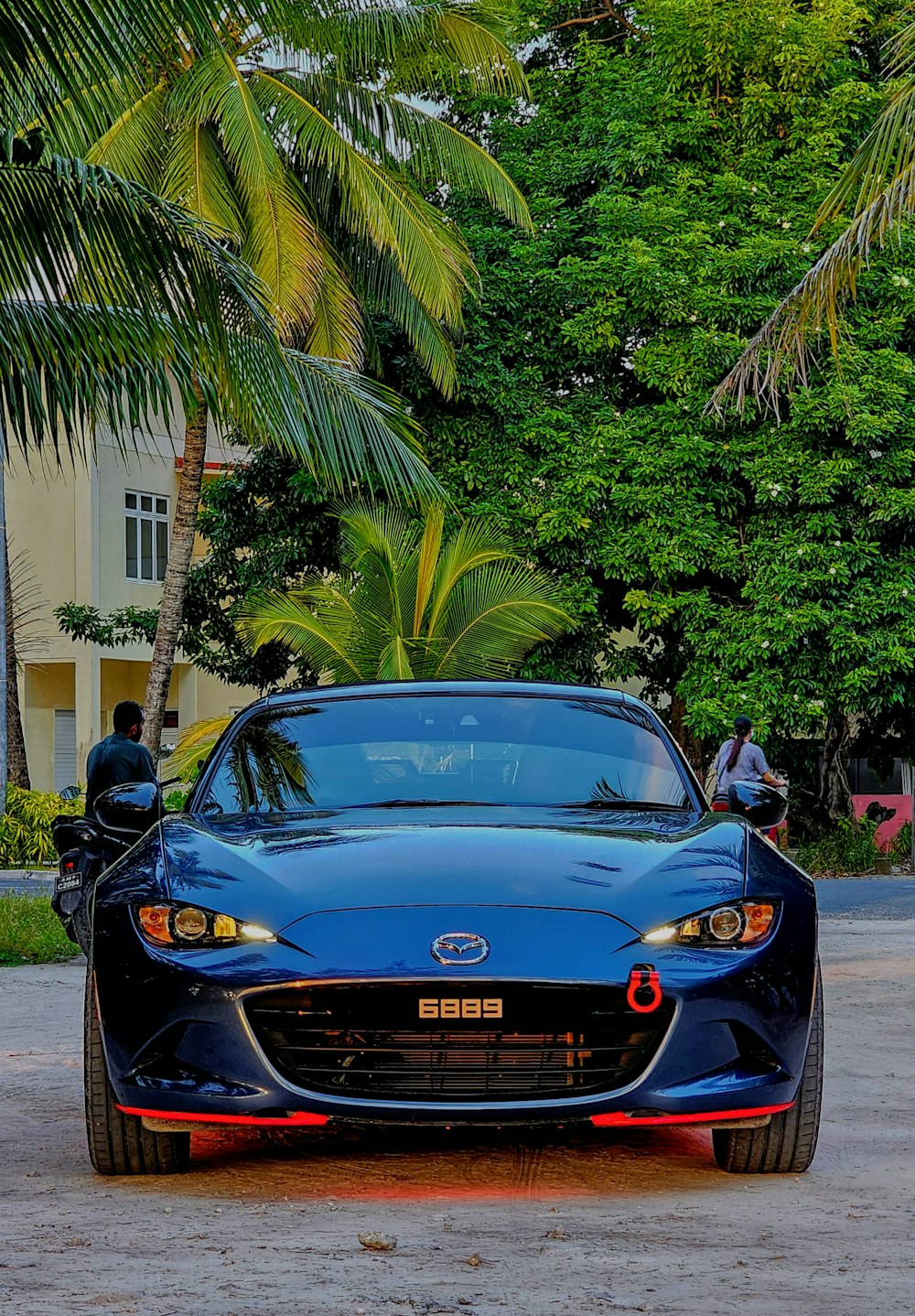 a blue sports car parked in front of a palm tree