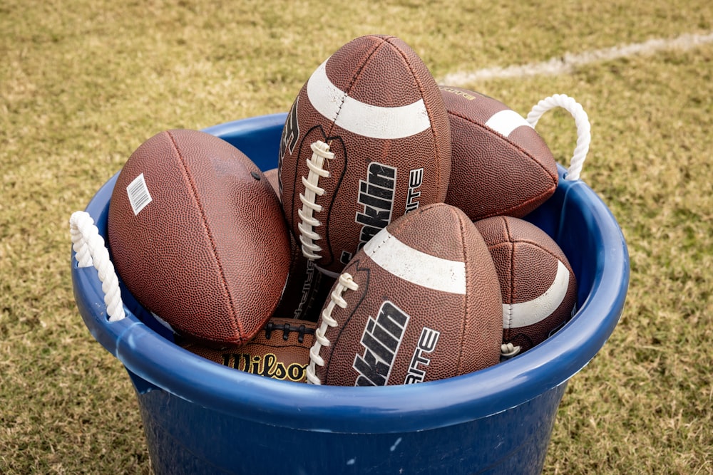a blue bucket filled with footballs on top of a field