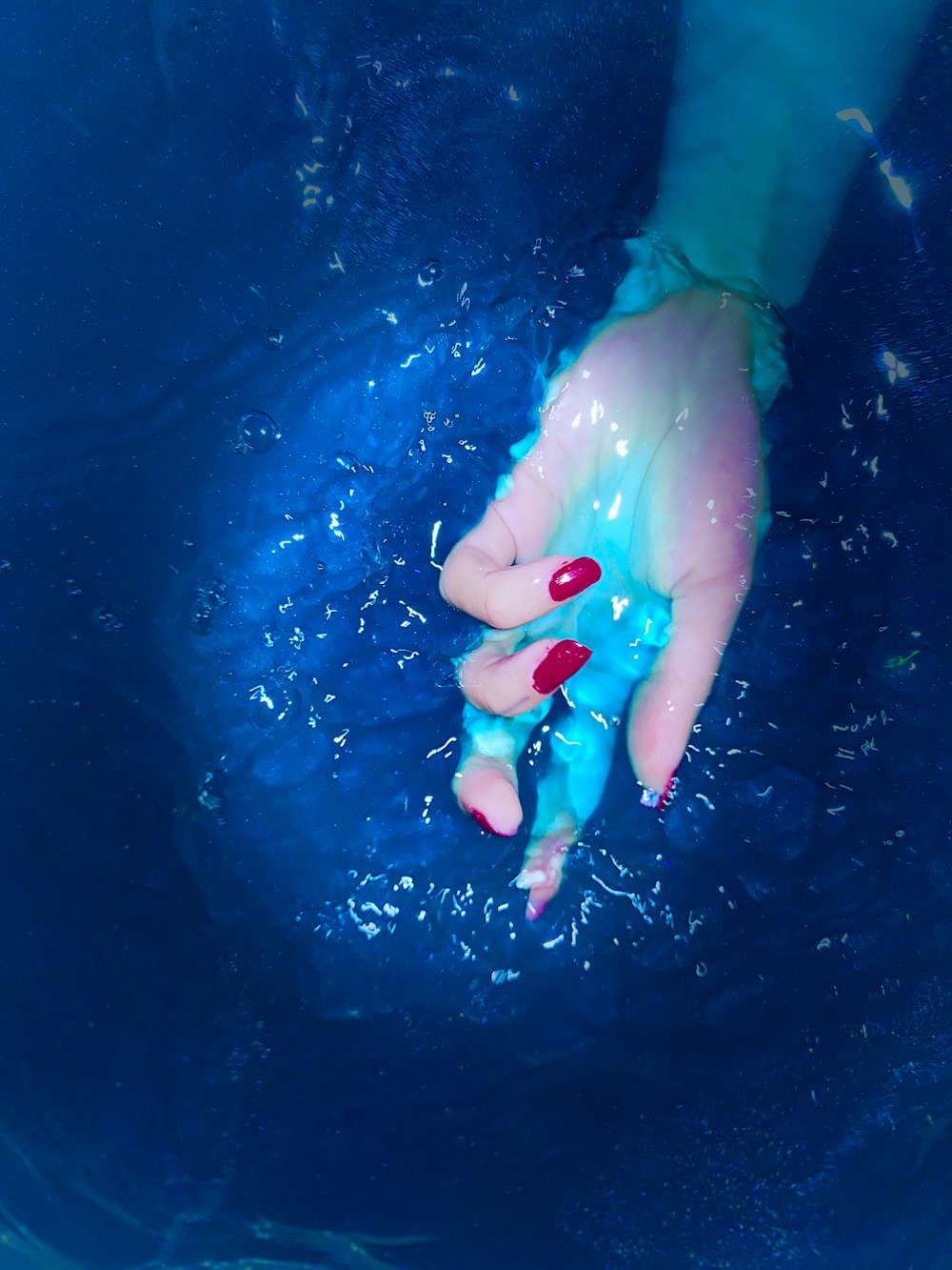 a person's hand in the water with red nail polish