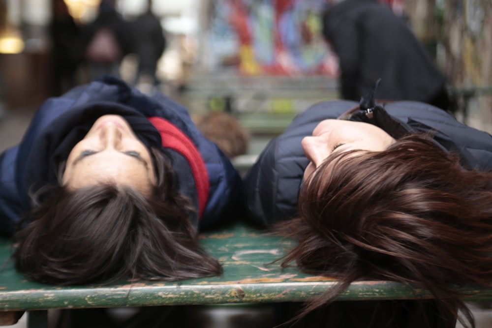 two women laying on a bench with their heads on each other