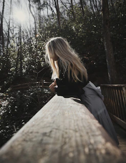 a woman sitting on a wooden bench in the woods