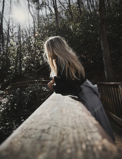 a woman sitting on a wooden bench in the woods