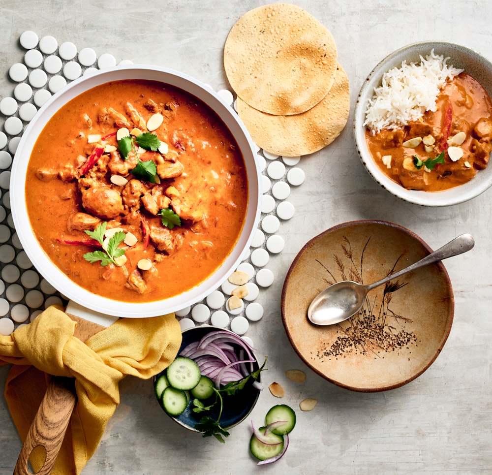 a bowl of red curry next to a bowl of rice and a bowl of soup