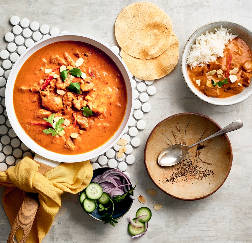 un bol de curry rouge à côté d’un bol de riz et d’un bol de soupe