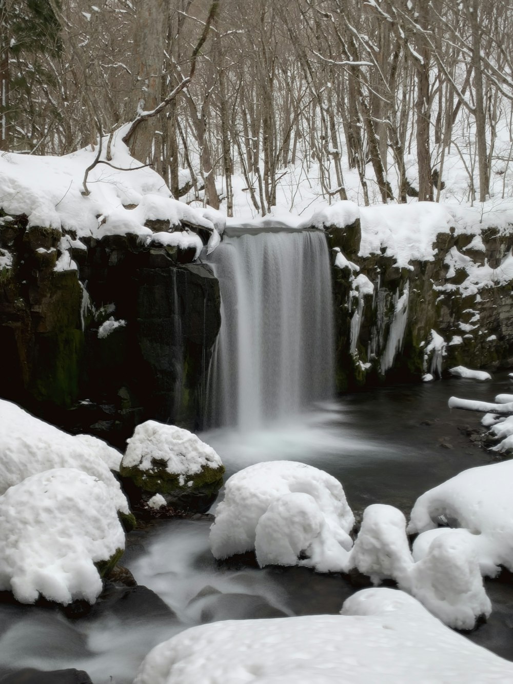 uma pequena cachoeira cercada por rochas cobertas de neve