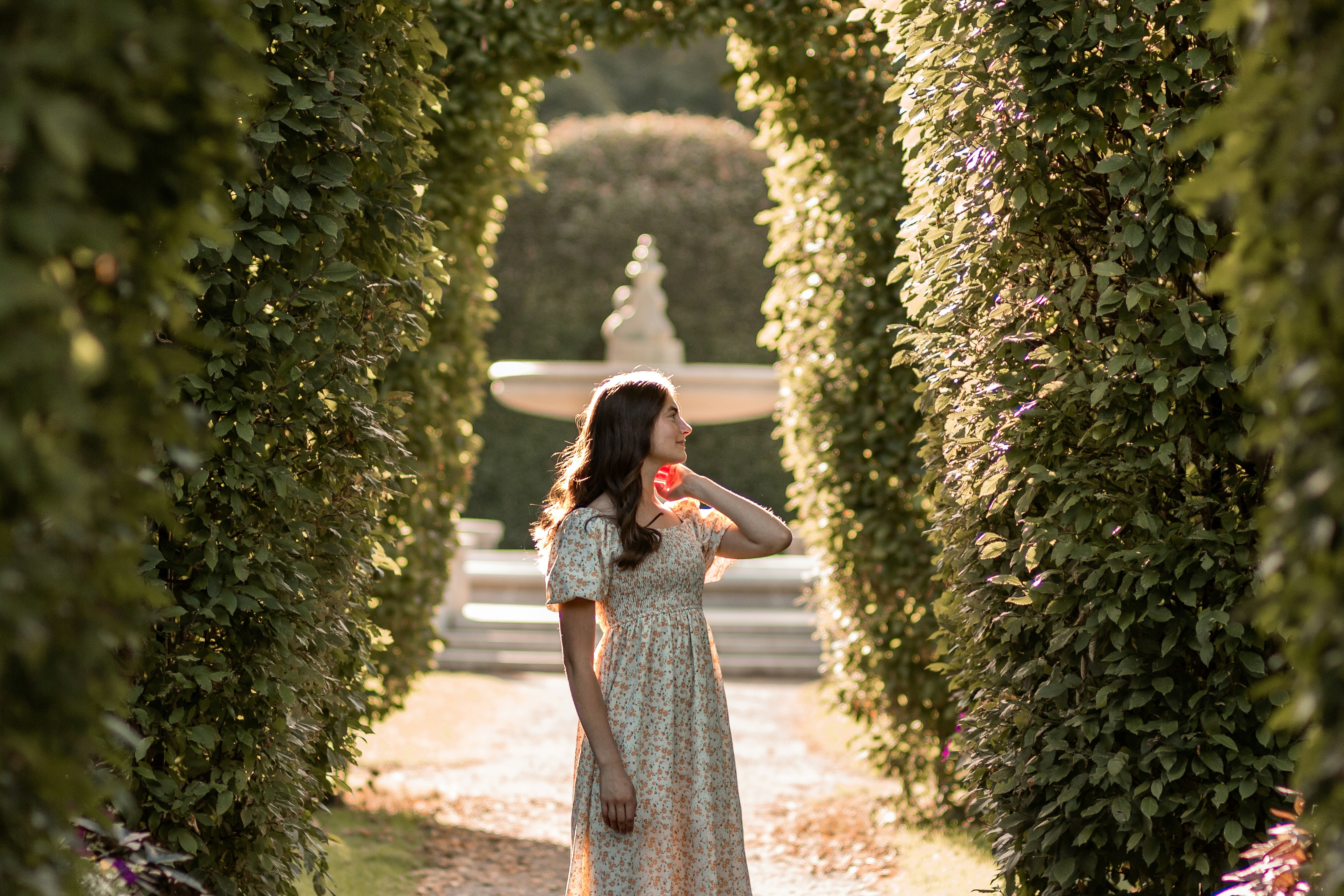 a woman in a dress walking through a tunnel of trees
