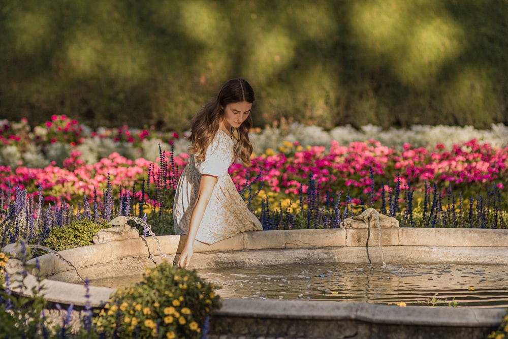 a little girl standing in front of a fountain surrounded by flowers