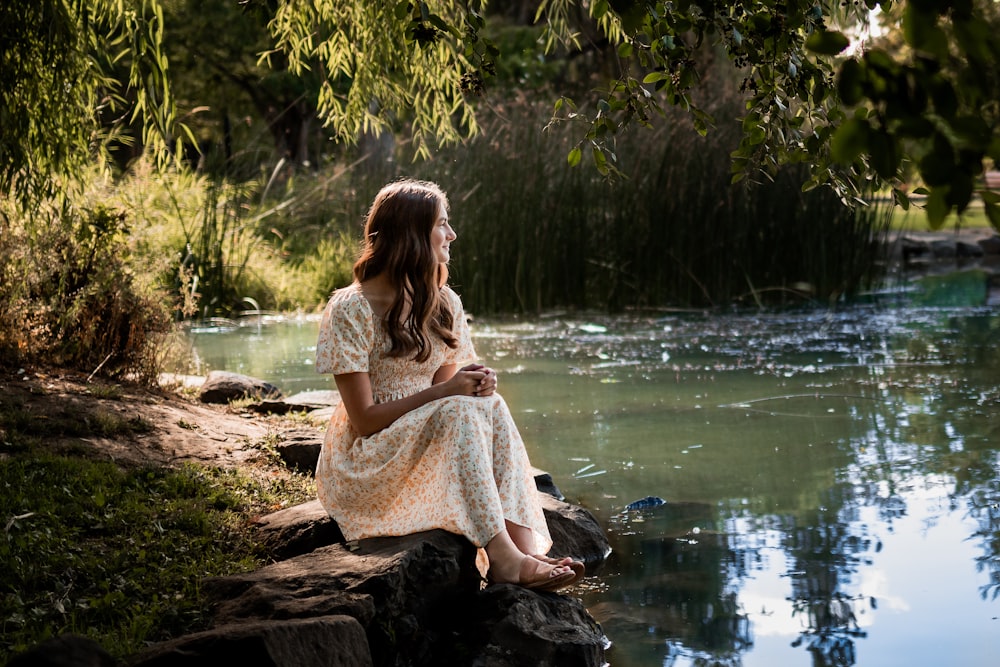 a woman sitting on a rock next to a body of water