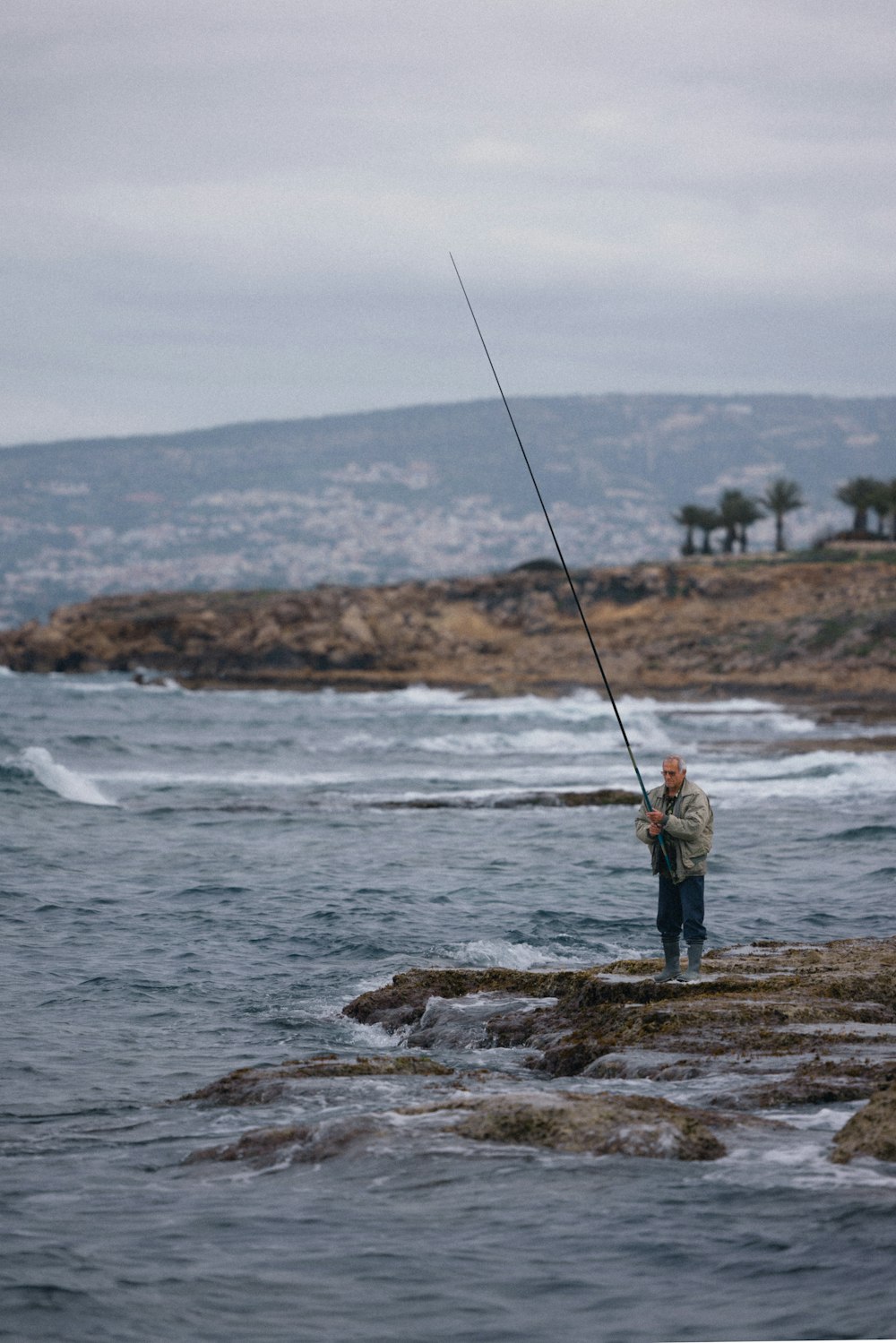 um homem em pé sobre uma rocha com uma vara de pesca