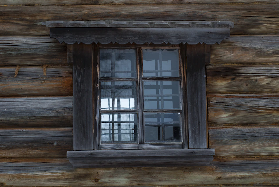 Close-up view of old wooden cabin with large rectangular window on the right side