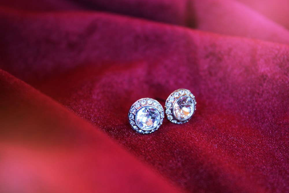 a pair of diamond earrings sitting on a red cloth
