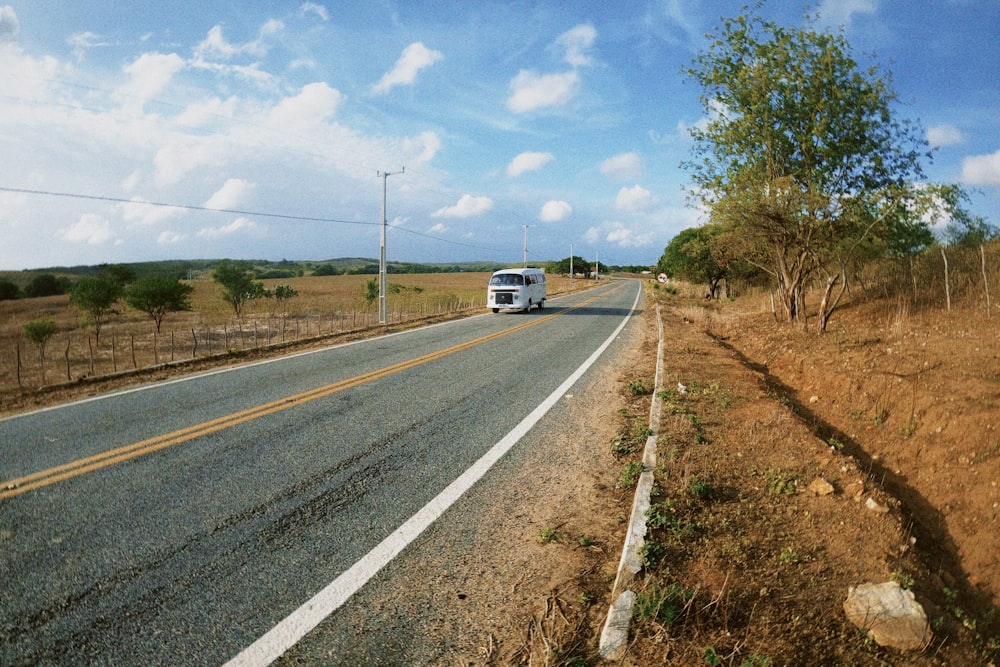 a white bus driving down a rural road