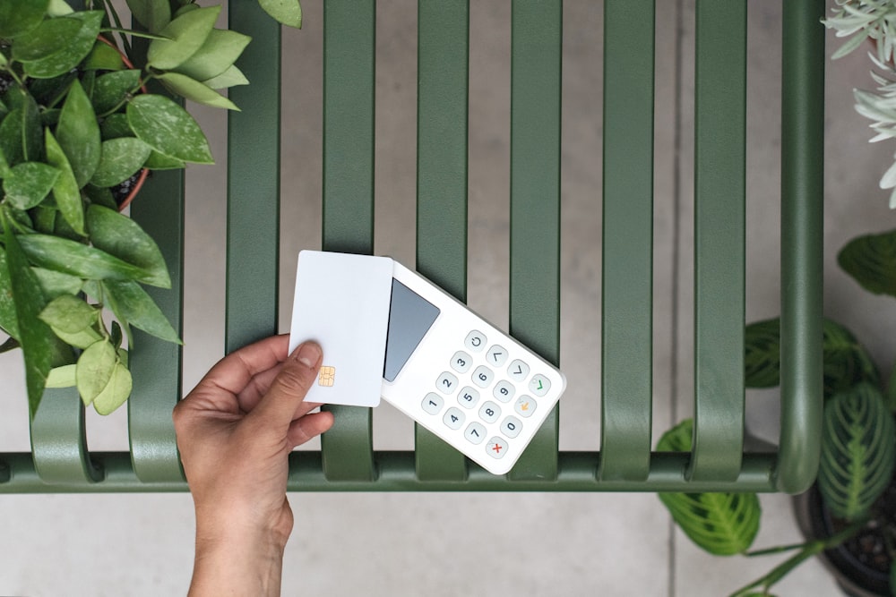 a person holding a remote control next to a green bench