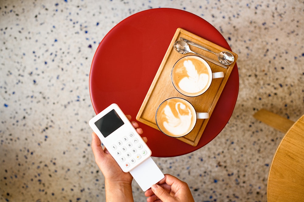 a person holding a cell phone next to a cup of coffee