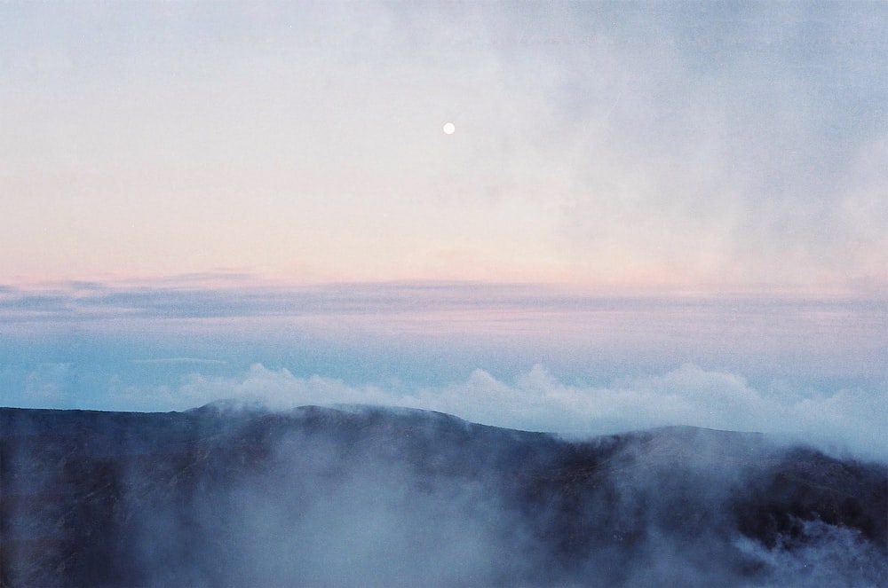 una montaña brumosa con una luna llena a lo lejos