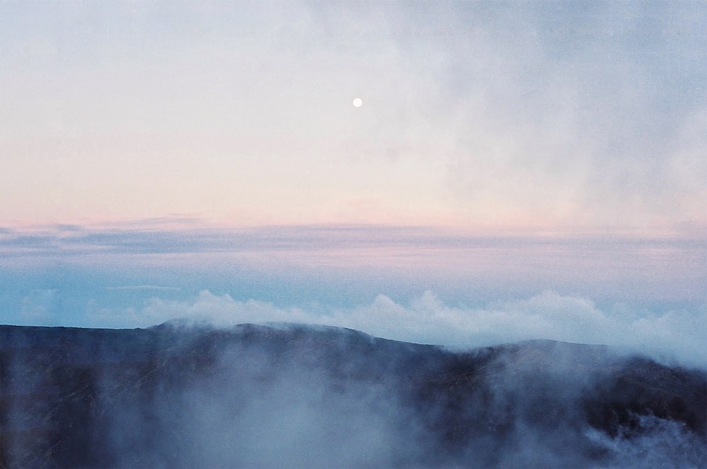 a foggy mountain with a full moon in the distance