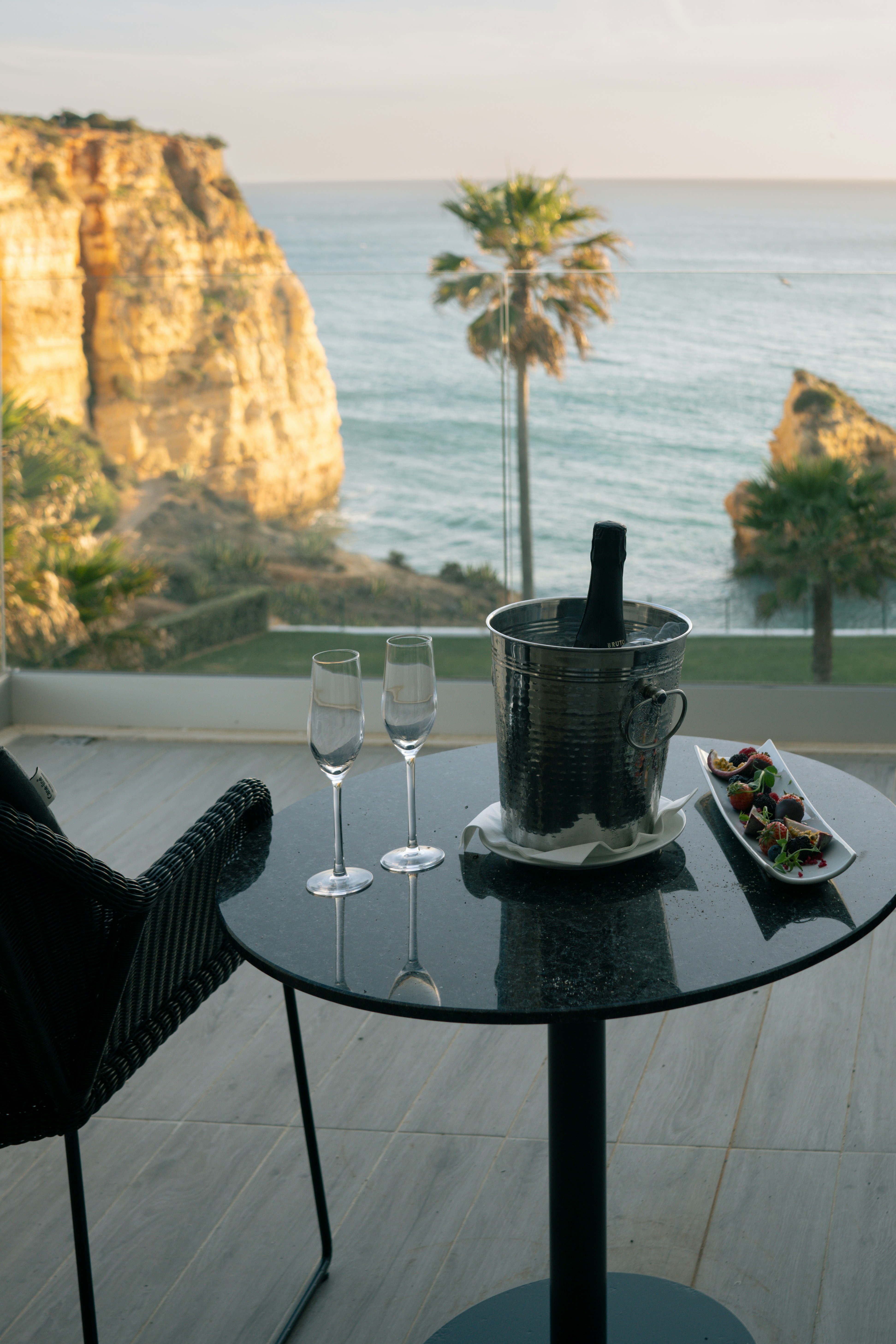 Fresh tropical fruit platter and champagne on white linen, ocean view through open villa doors, morning light streaming in