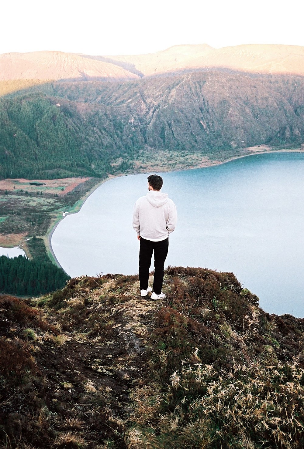 a man standing on top of a hill overlooking a lake