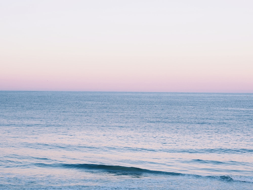 a large body of water sitting under a pink sky