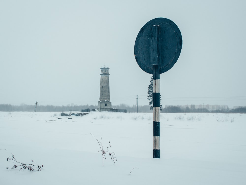 a sign in the snow with a light house in the background