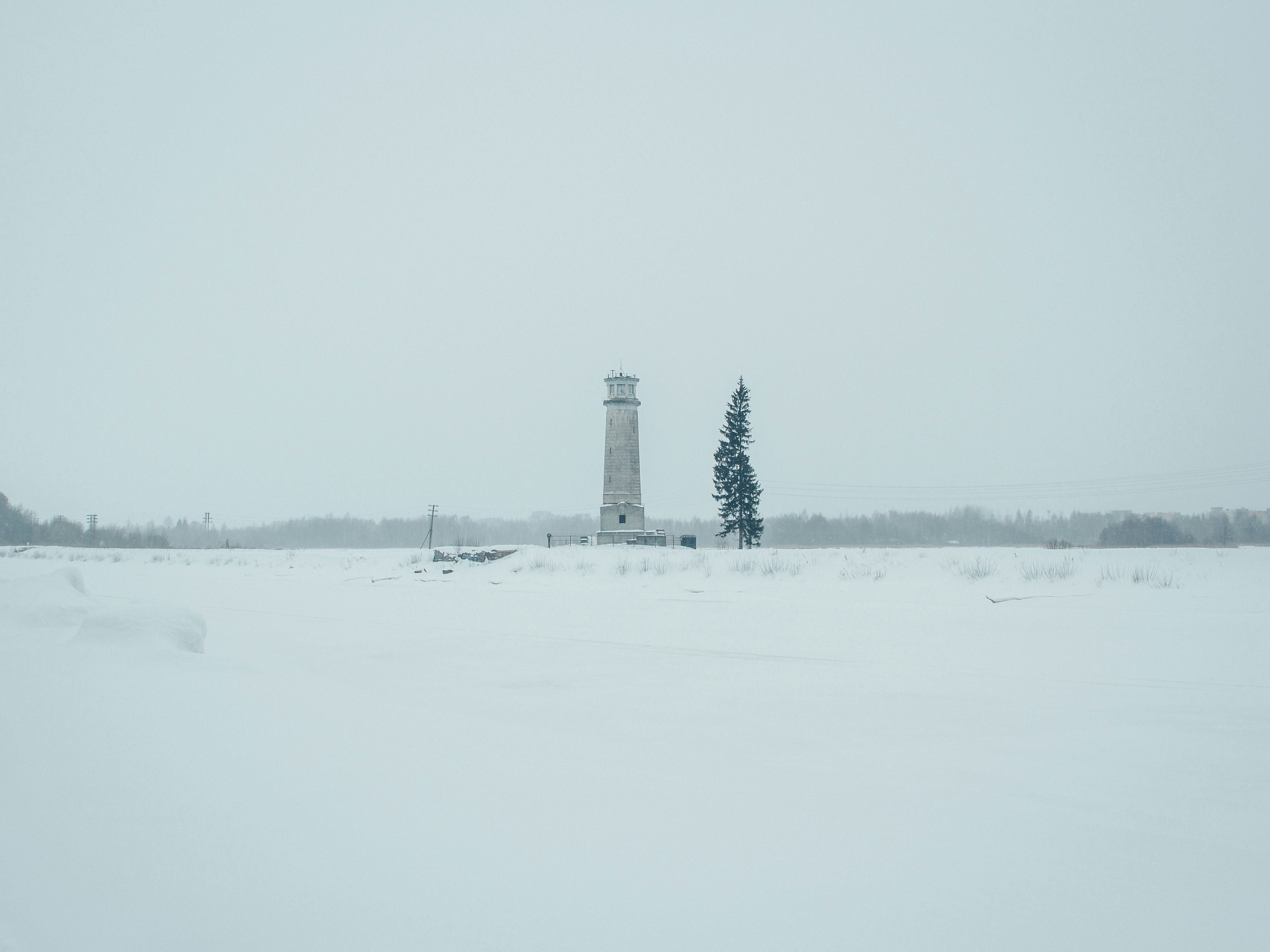 a snow covered field with a light house in the distance
