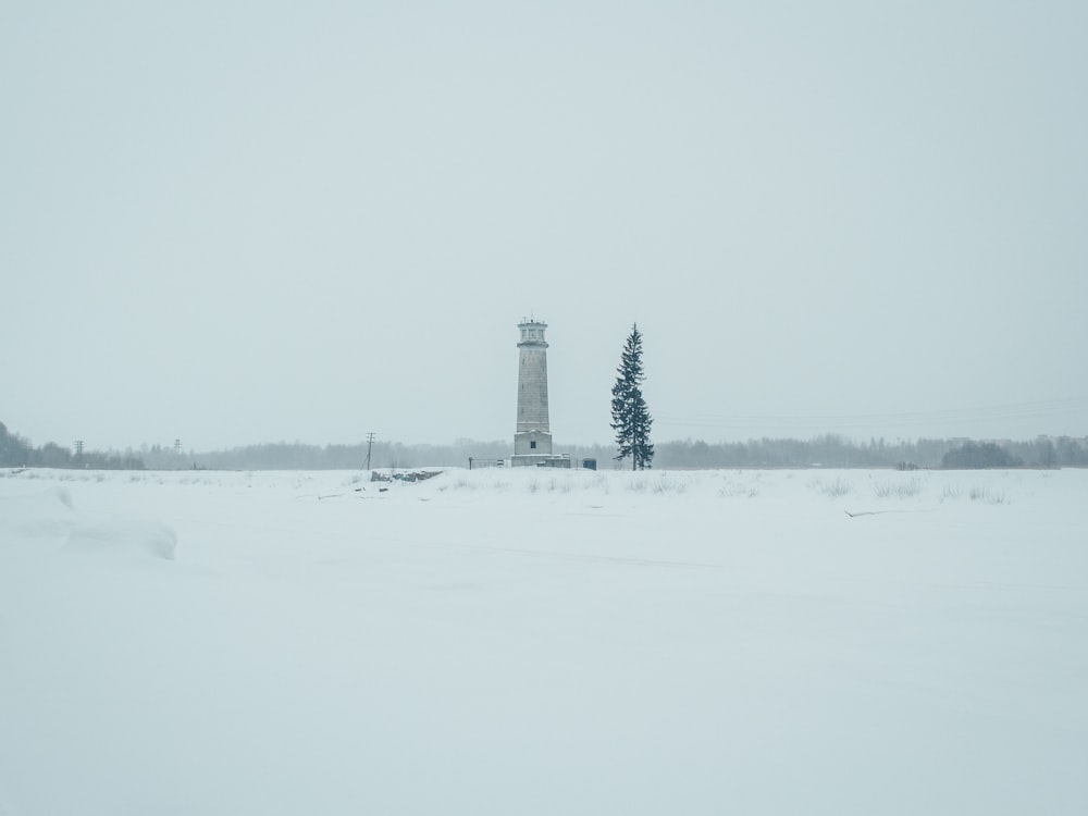 a snow covered field with a light house in the distance