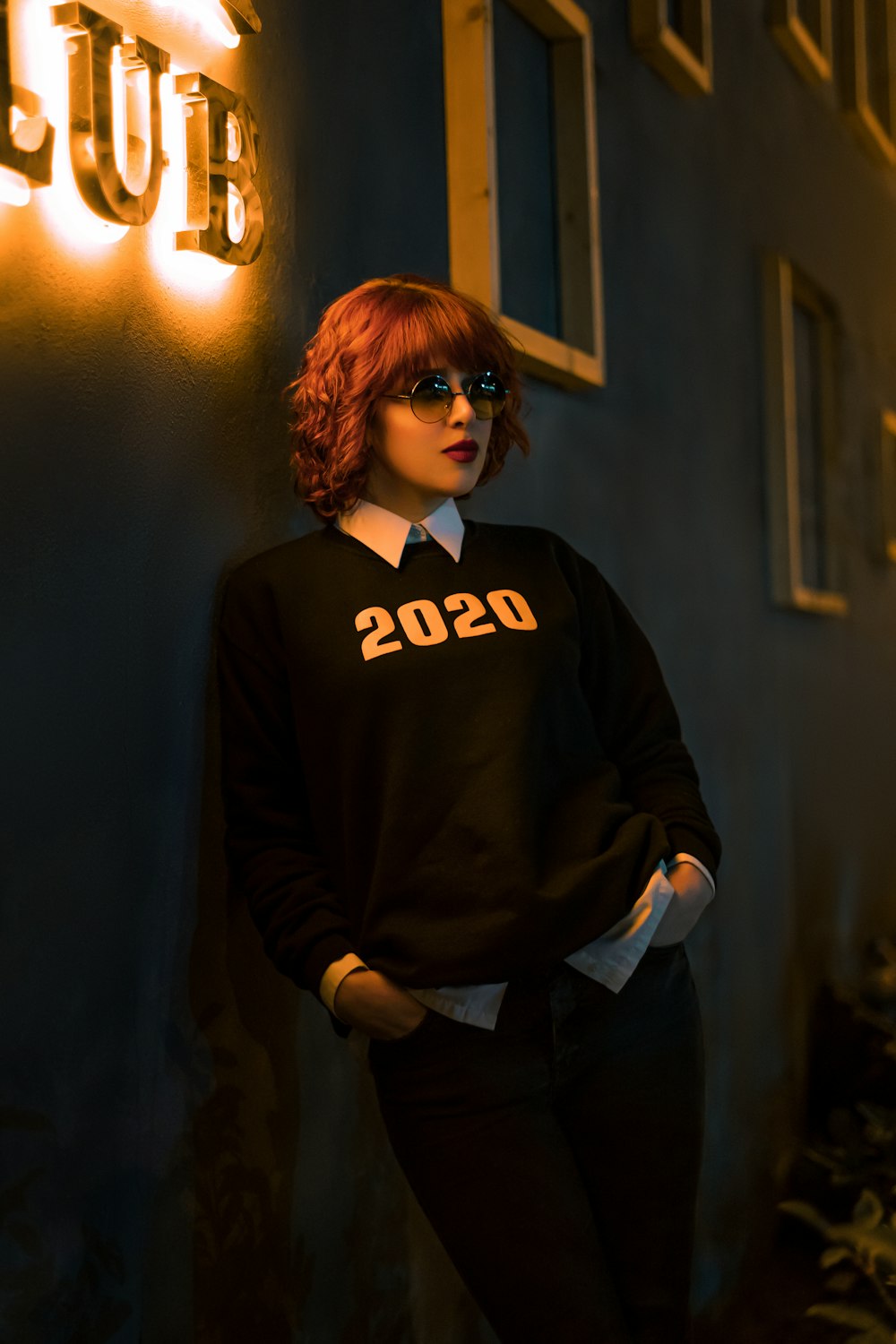 a woman standing next to a wall with a neon sign