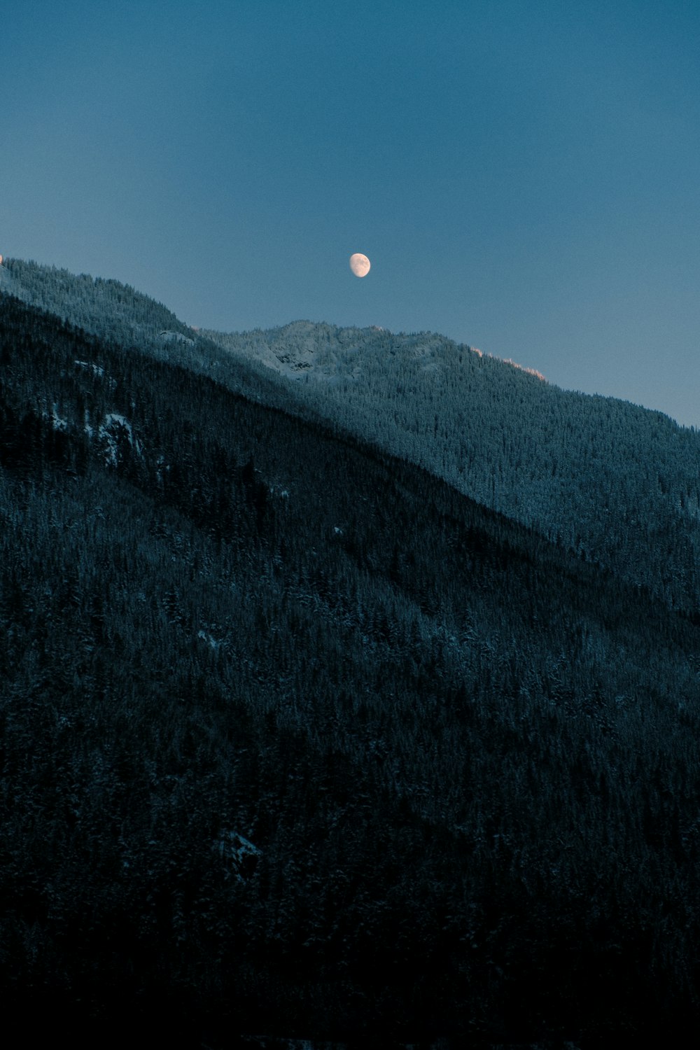 a full moon rising over a mountain range