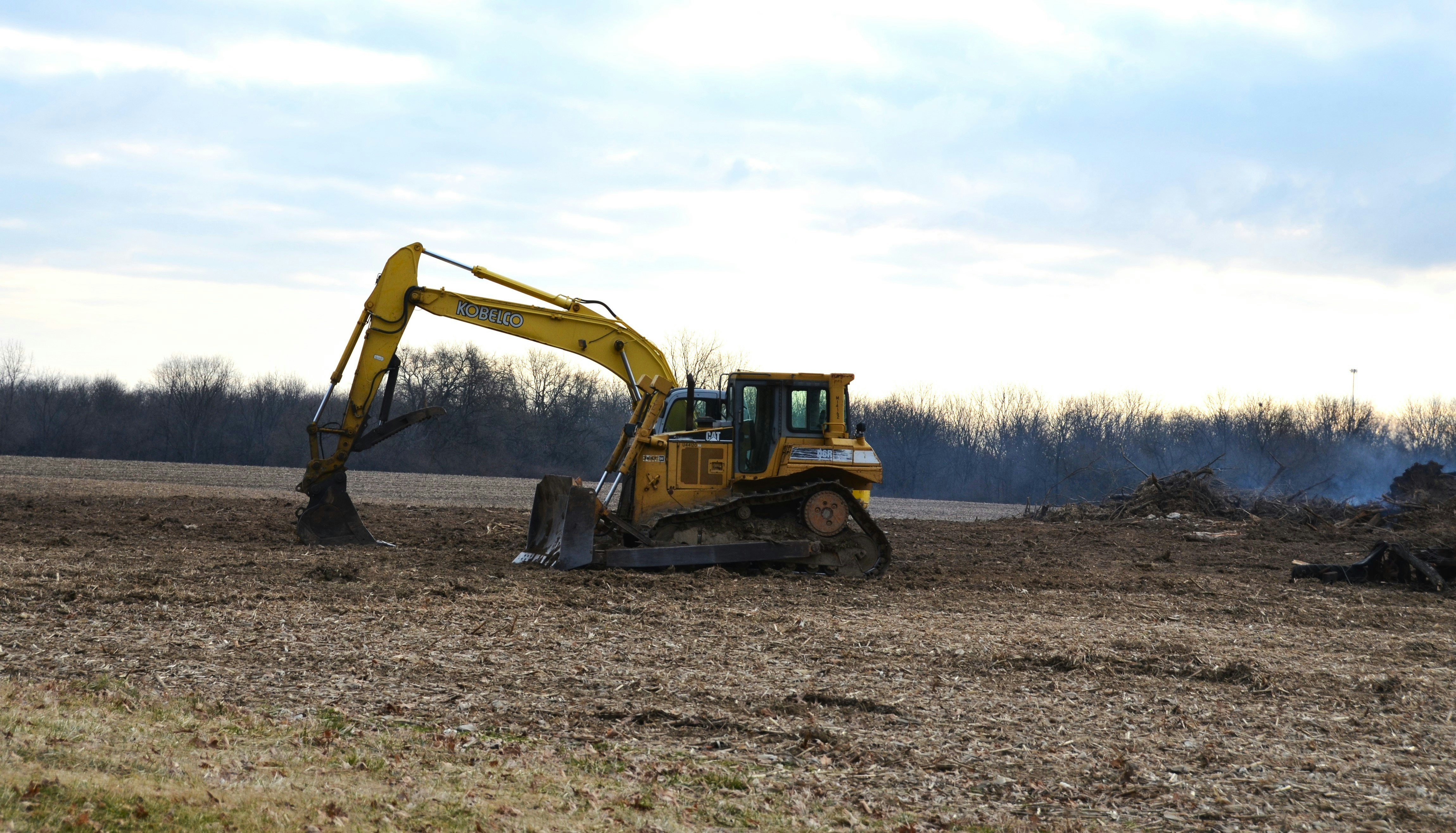 a bulldozer digging through a field with a sky background