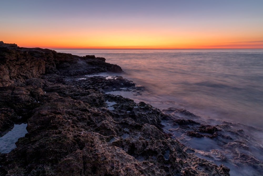 the sun is setting over the ocean on the rocky shore