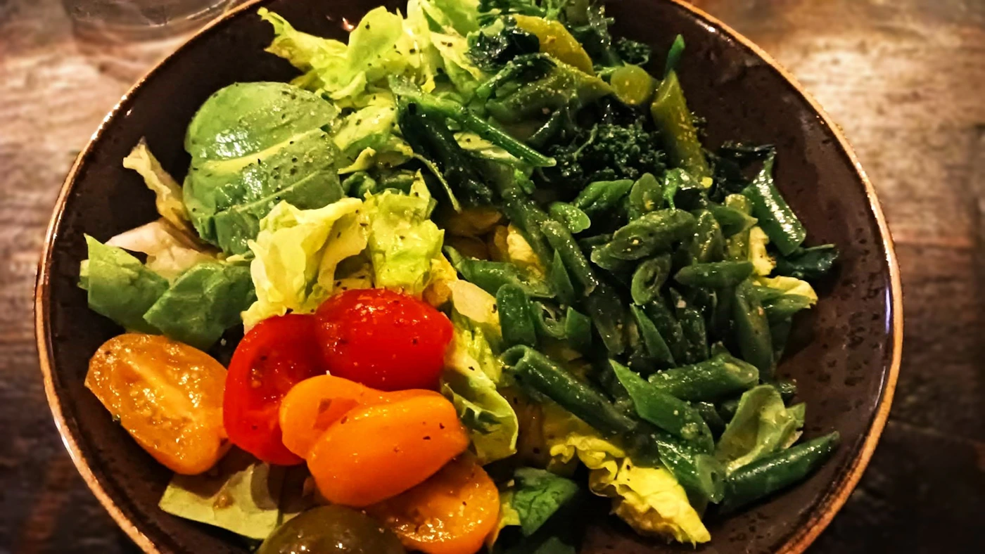 Prato real com folhas verdes, abacate, tomate e vagem sobre mesa de madeira