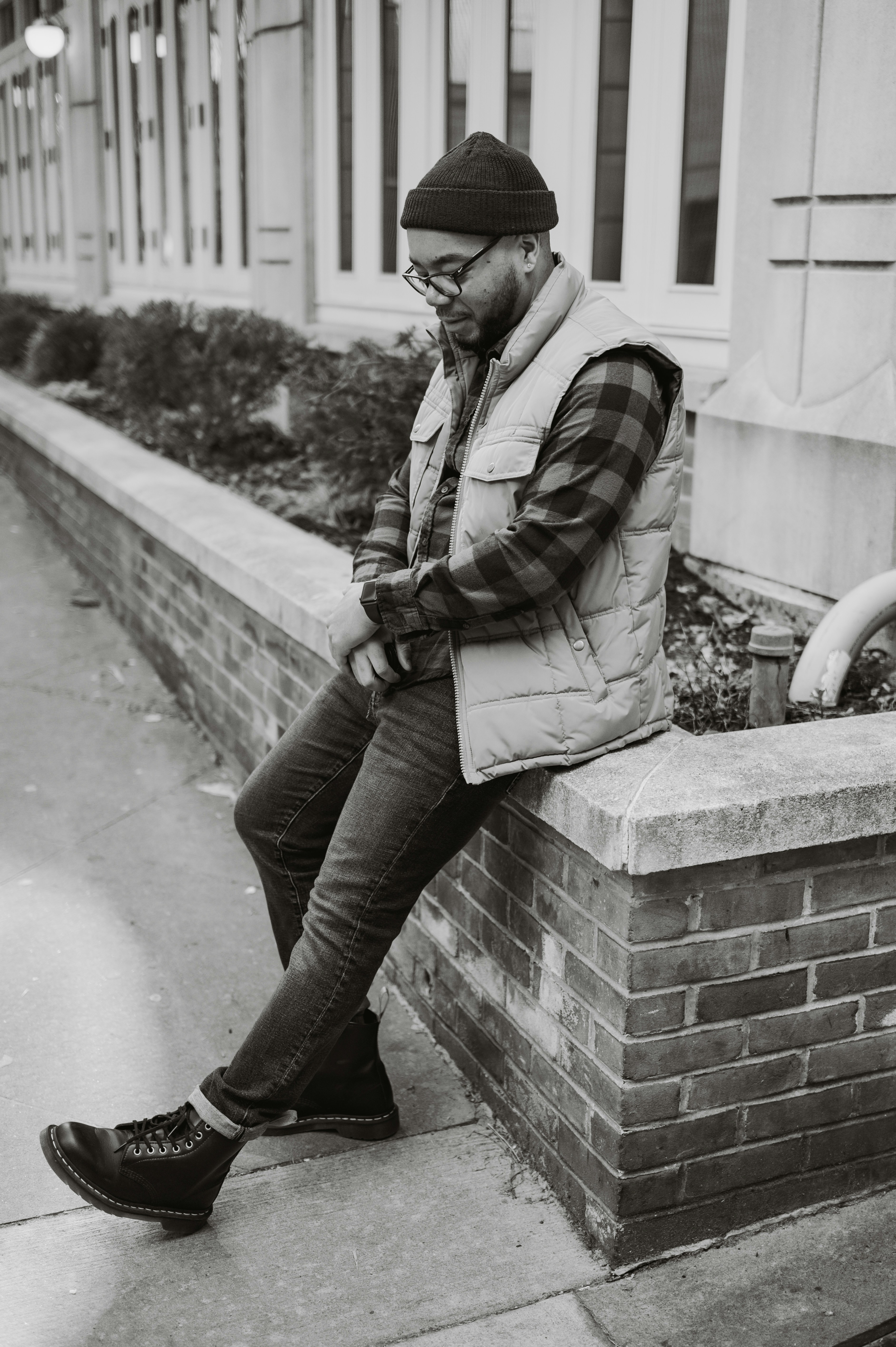 a black and white photo of a man sitting on a brick wall