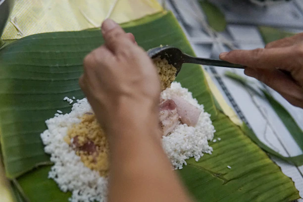a person cutting up food on a banana leaf