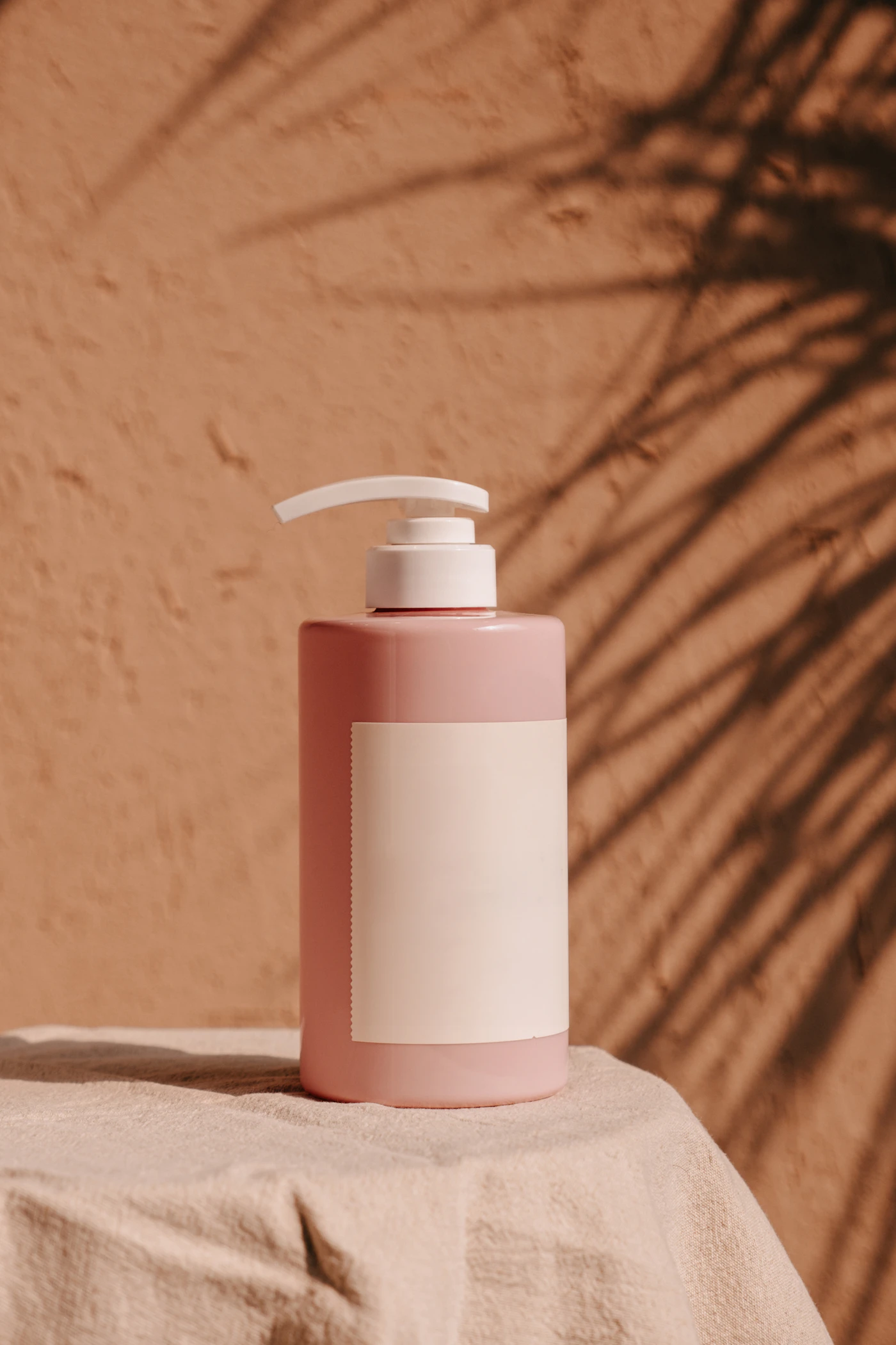 Blush pink pump bottle of hydrating lotion against a terracotta wall