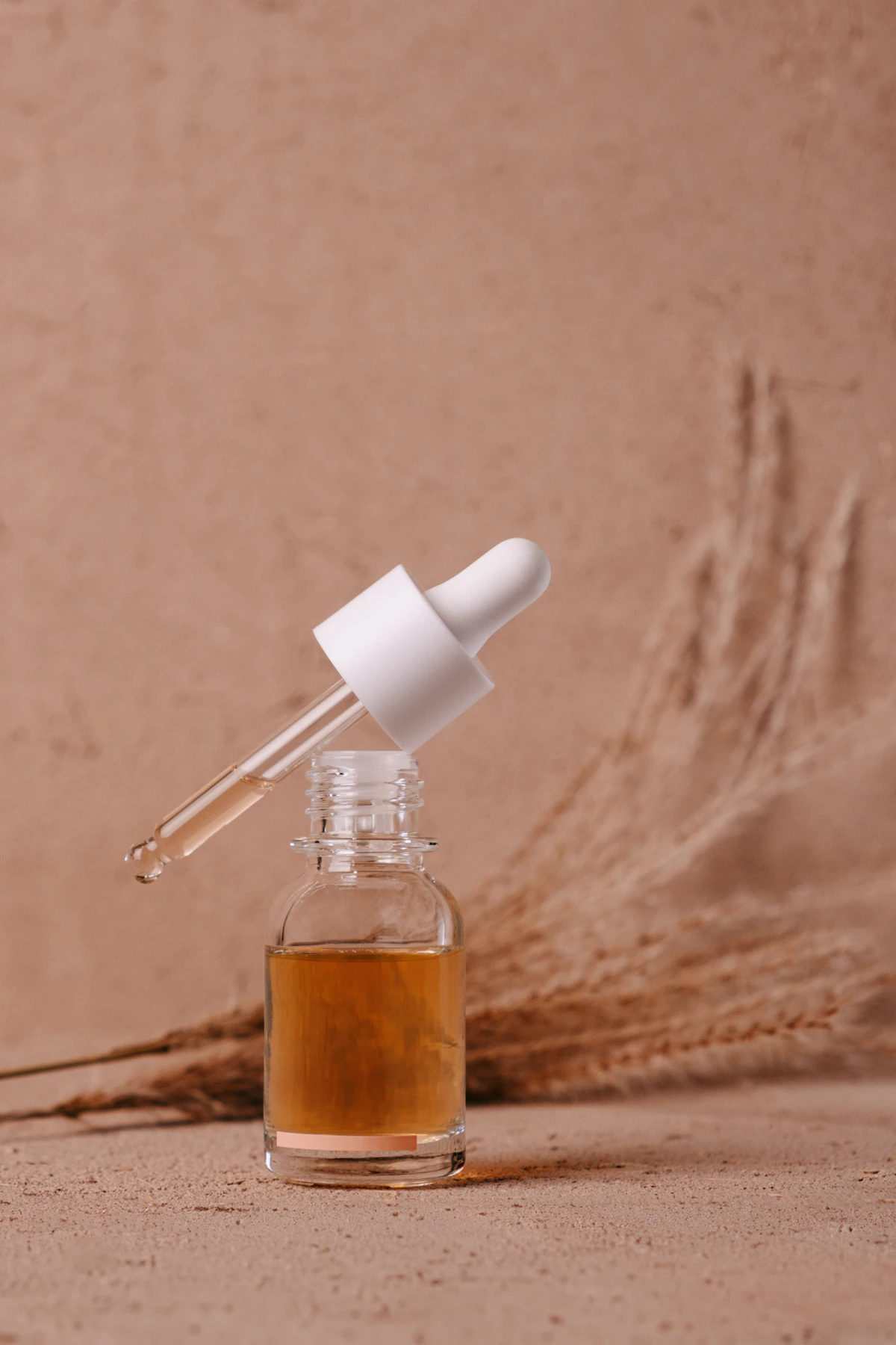 Glass dropper resting in an amber serum bottle against a sandy wall