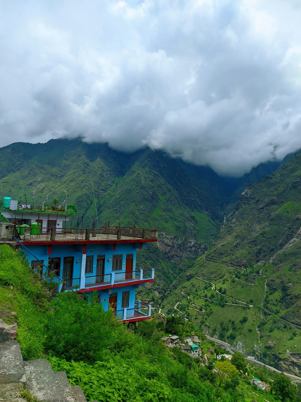 a blue and red building sitting on top of a lush green hillside
