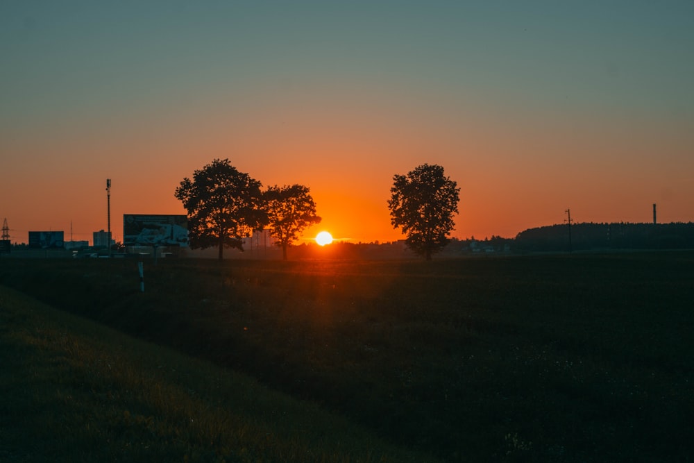 the sun is setting behind two trees in a field