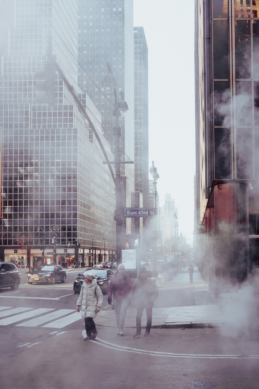 a group of people walking across a street next to tall buildings