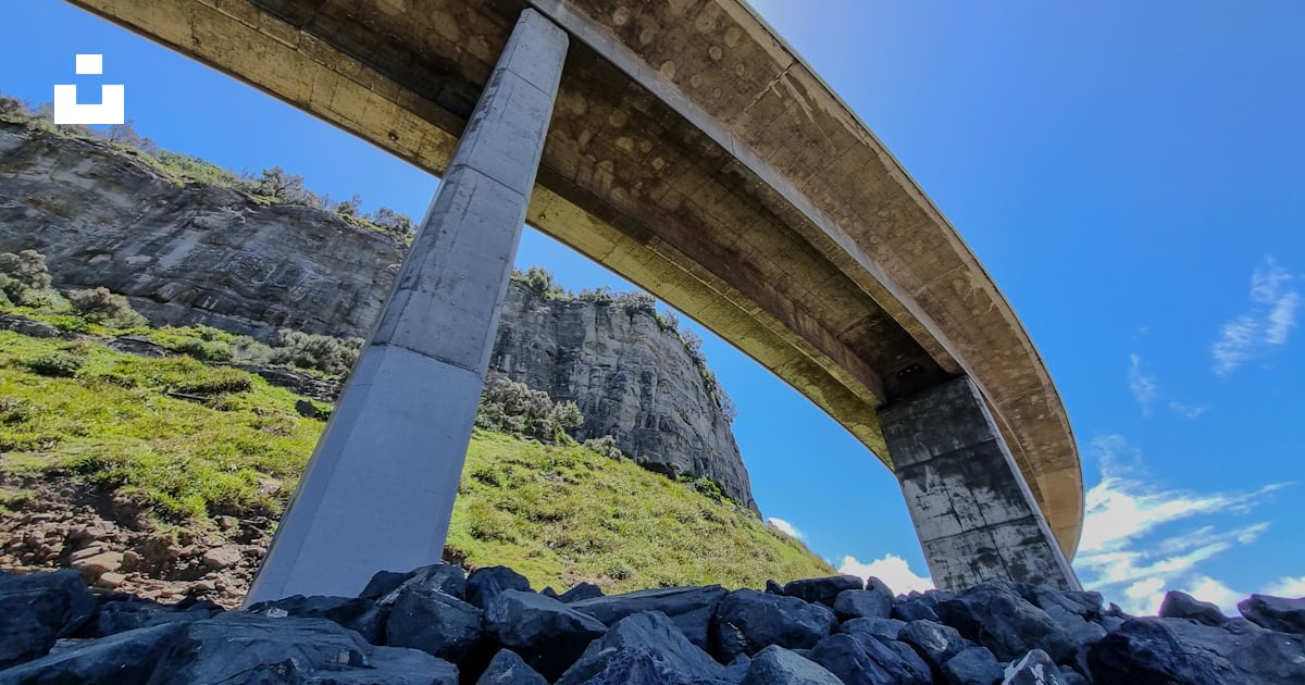 A view of a bridge over rocks with a rainbow in the sky photo – Free ...