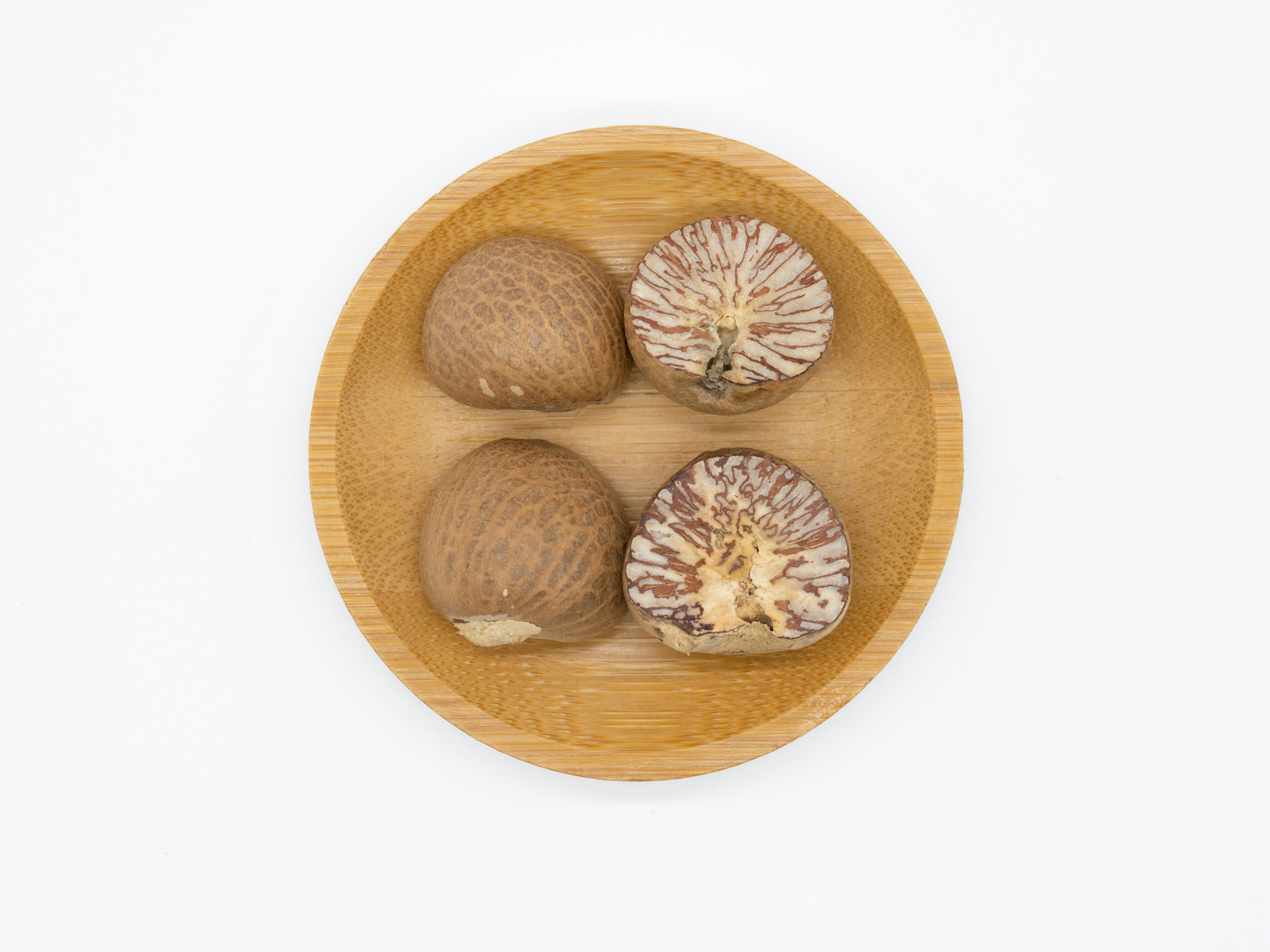 Whole nutmeg seeds and ground nutmeg powder in wooden bowl showing brown aromatic spice
